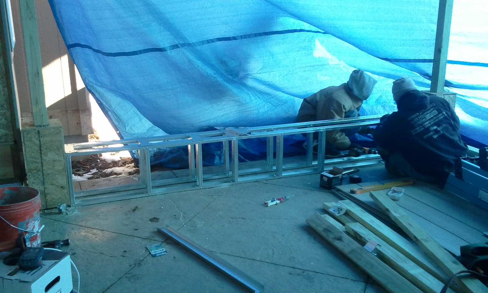 Two workers installing metal framing under blue tarp