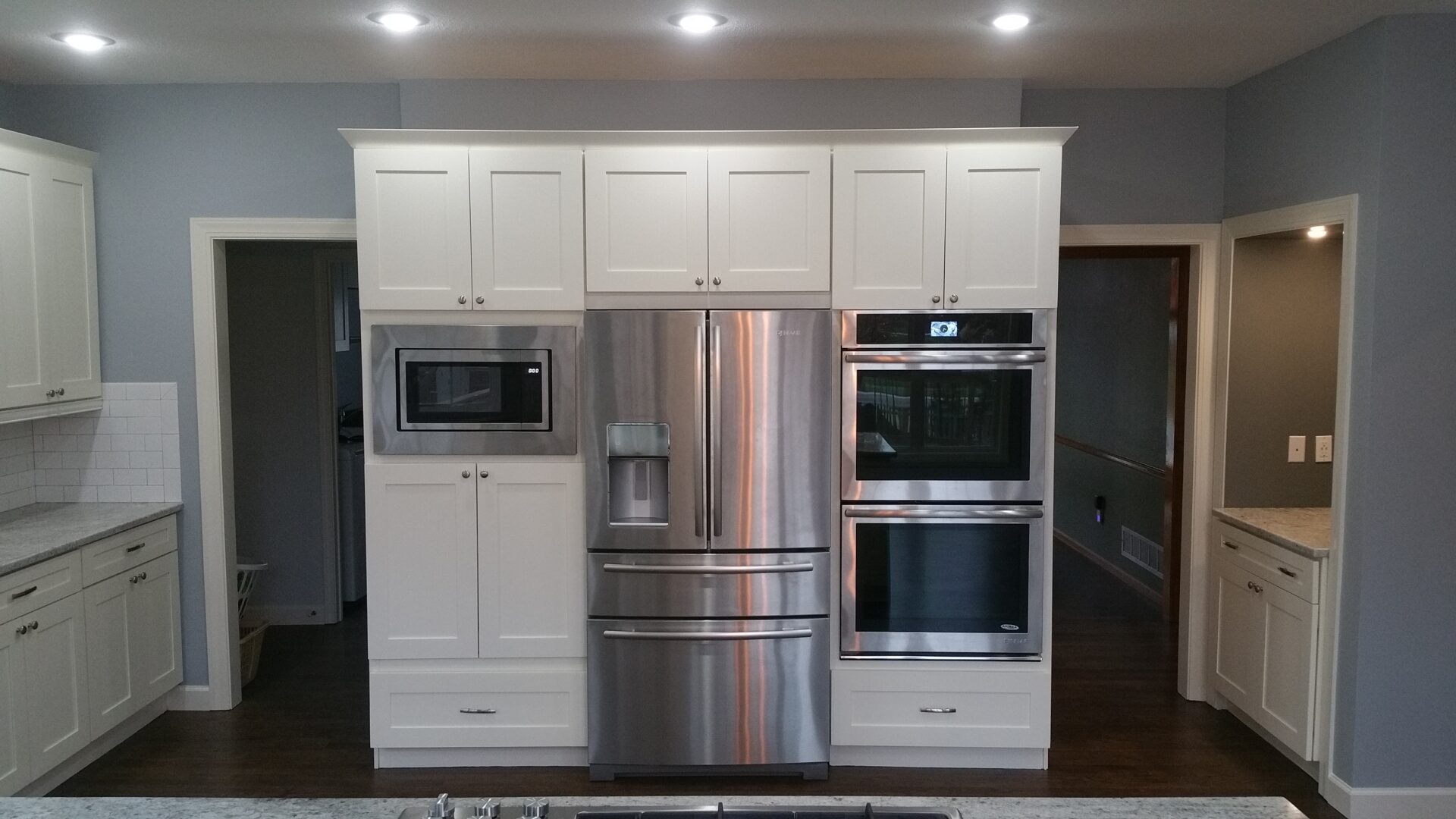 White kitchen cabinetry with stainless refrigerator and ovens