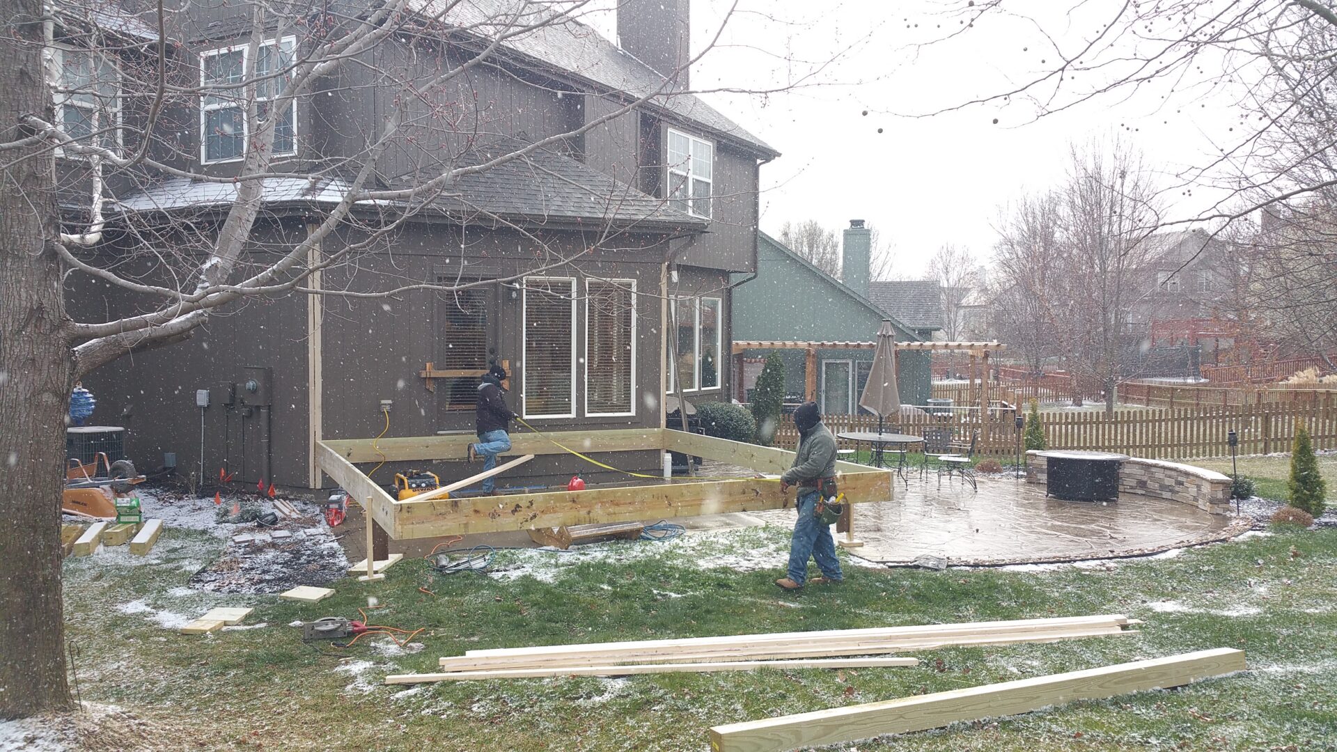 Workers building wooden deck in snowy backyard