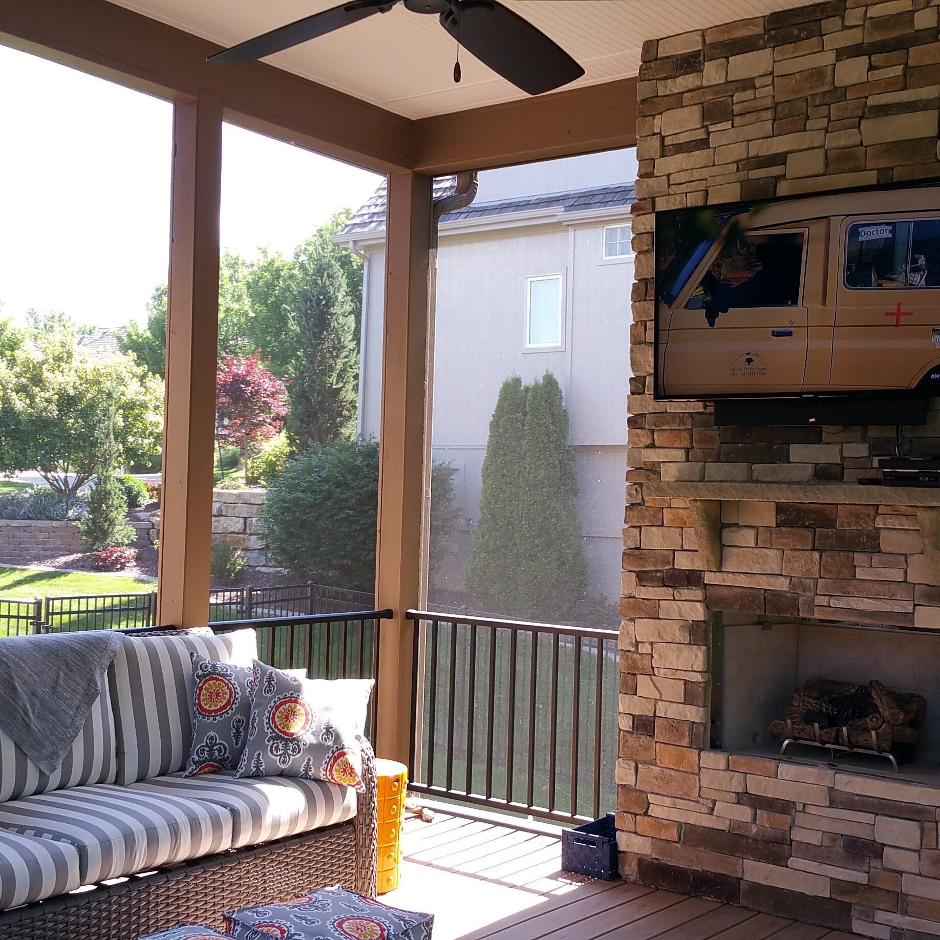Cozy porch with striped sofa and brick fireplace overlooking a sunny garden.